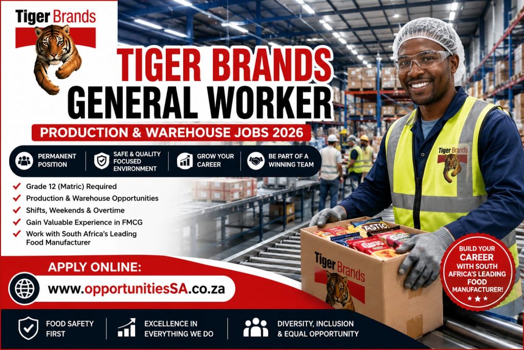 A professionally dressed Tiger Brands production and warehouse employee wearing PPE while handling packaged food products inside a clean, modern manufacturing facility with pallets, inventory, and warehouse shelving in the background.